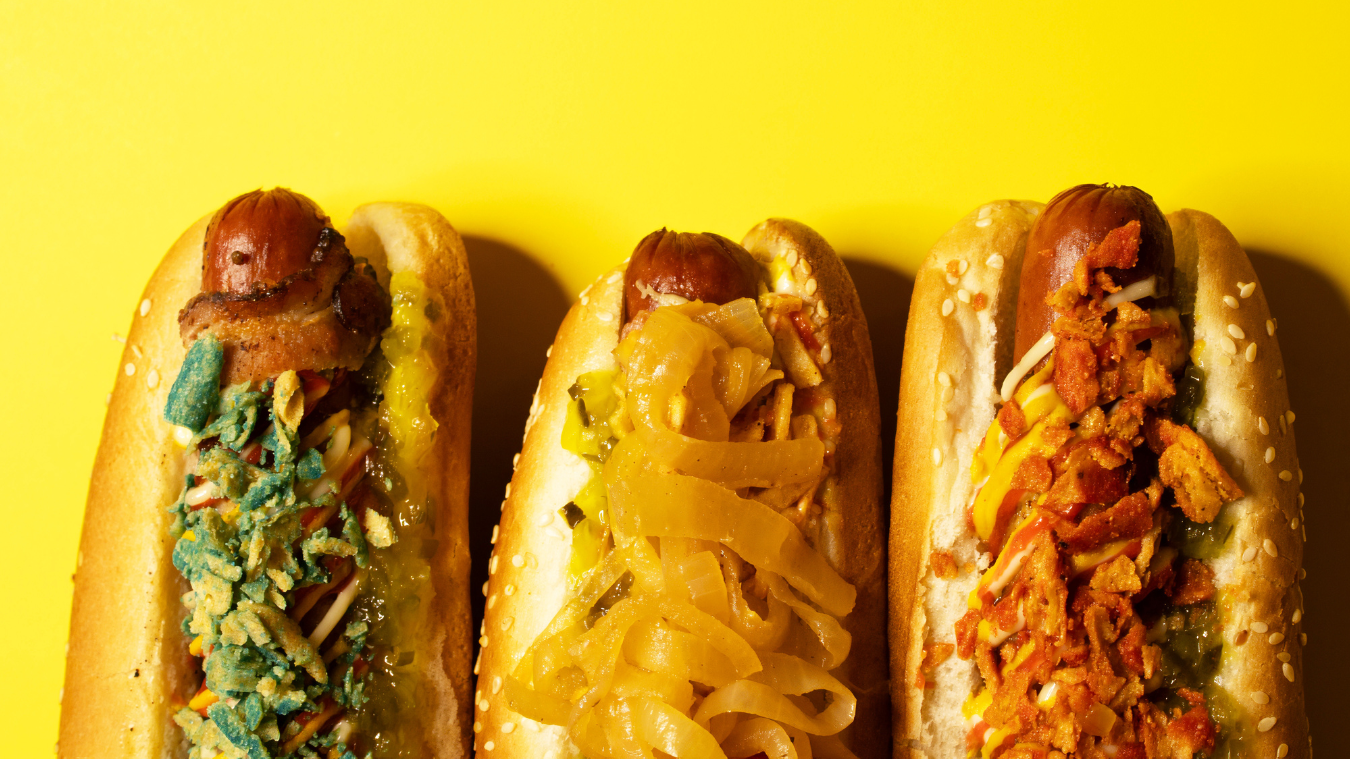 Three hot dogs with different toppings on a yellow background